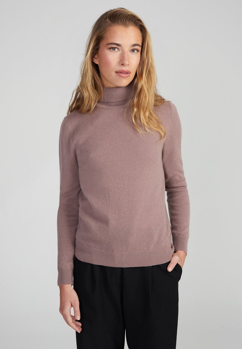 Helllila Rollkragenpullover aus weichem Strickstoff mit gerippten Bündchen und Saum, kombiniert mit lockeren schwarzen Hosen.