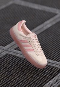 Helle rosa Wildleder-Sneaker mit drei pinken Streifen, strukturiertem Gummisohle und kontrastierenden pinken Akzenten an Ferse und Zunge.