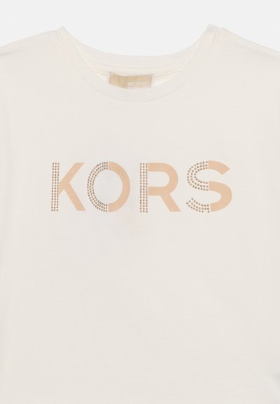 T-shirt col rond couleur crème avec le texte "KORS" en marron clair, agrémenté de petits clous métalliques formant une partie des lettres à l'avant.