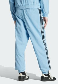 Light blue tracksuit pants made of lightweight fabric, featuring three black side stripes and elastic cuffs, paired with black sports shoes.