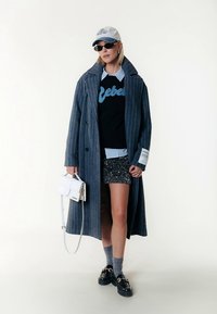 Dugi plavi kaput s prugama preko crnog džempera s natpisom "Rebel" i kratkih šljokičastih hlača. Modni dodaci uključuju bijelu torbicu, kapu i sunčane naočale.