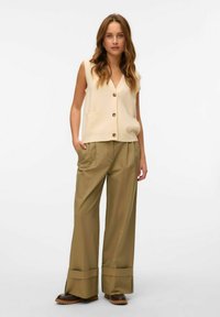 Caraco sans manches beige avec trois boutons et poches, associé à un pantalon ample kaki avec un ourlet à revers et un tissu texturé.