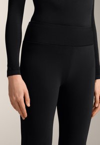 Čierne legíny s elastickým strihom a hladkým textilom, majú široký pás. Sú navrhnuté tak, aby priliehali na telo, pričom nemajú viditeľné švy.