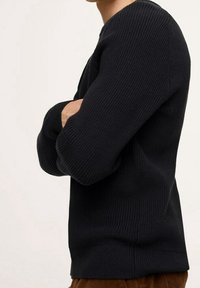 Pull en maille côtelée noir avec un col rond et des manches longues ; présente une coupe décontractée et un tissu texturé. Aucun logo ou motif visible.