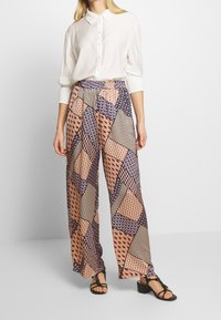 Kraťasy širokého střihu v barevném geometrickém vzoru s odstíny růžové, modré a béžové; lehký materiál; elastický pas; spárováno s bílou blůzou.