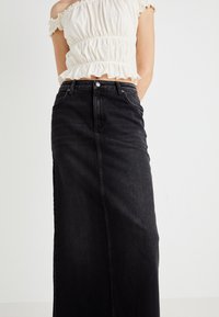 Black denim maxi skirt with a straight design, high waist, and front button closure. Features a smooth texture and minimal stitching details.
