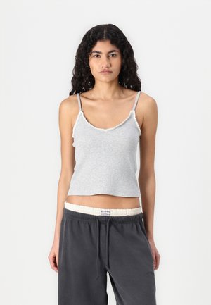 Graues ärmelloses Oberteil mit V-Ausschnitt, Rüschensaum und dünnen Trägern, kombiniert mit dunkelgrauen Sweatpants mit Kordelzug.