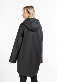 Impermable negro con capucha, con un corte holgado, mangas largas y cierres a presión en los puños. Textura suave y un diseño minimalista.