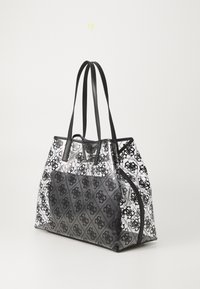 Sac fourre-tout transparent avec des accents noirs à motifs. Il présente deux poignées noires, une fermeture éclair et un design de logo géométrique à l'avant.