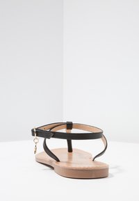 Černé sandály na ploché podrážce s tenkými pásky, s hnědou stélkou a jemným kovovým detailem. Minimalistický design s otevřenou špičkou.