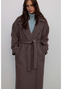 Długi, brązowy płaszcz z pasek w talii, dużymi klapami i podwójnym zapięciem na guziki. Wykonany z teksturowanej, ciepłej tkaniny z bocznymi kieszeniami.