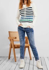 Felpa a maniche lunghe color crema con strisce orizzontali blu e verdi, dotata di cappuccio con coulisse. Abbinata a jeans blu chiaro e sneaker bianche.