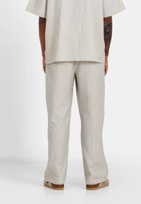 Ensemble en deux pièces en coton rayé comprenant un haut à coupe décontractée et un pantalon. Palette de couleurs neutres avec des rayures verticales, silhouette décontractée.