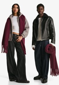 Grå och burgundy lager på lager ytterkläder med fransar, vit skjorta, vida mörka jeans och svart läderjacka, tillsammans med en matchande burgundy hatt.