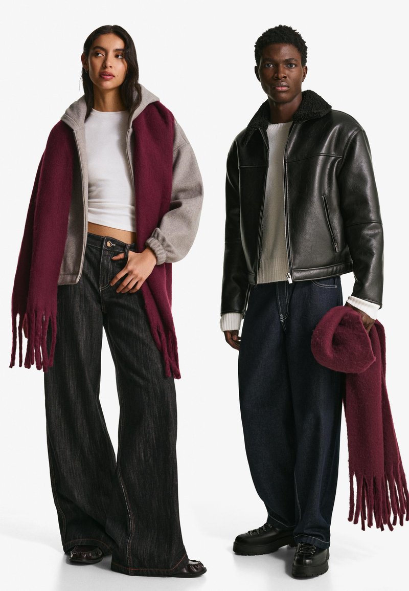 Grå och burgundy lager på lager ytterkläder med fransar, vit skjorta, vida mörka jeans och svart läderjacka, tillsammans med en matchande burgundy hatt.