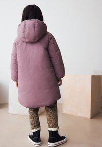 Kohev tuulejope helelilla kapuutsiga, pikkade varrukatega, kombineeritud leopardimustriliste pükste ja mustade kõrgete tennistega.