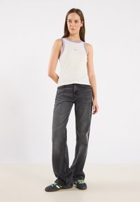 Vit linne med lila kant och logotyp; matchat med mörkgrå vida jeans och svarta skor med gröna detaljer.