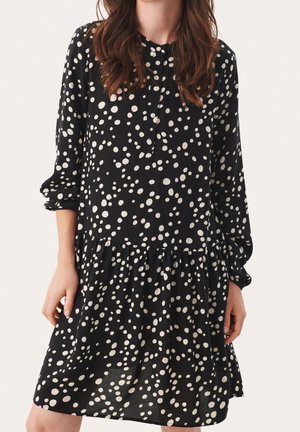 Robe noire à pois blancs, manches longues, patte de boutonnage et ourlet à volants en couches. Fabriquée en tissu léger.
