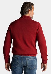 Rode gebreide trui met een hoge geribbelde kraag, een gestructureerde stof en geribbelde manchetten, gecombineerd met lichtblauwe spijkerbroek.