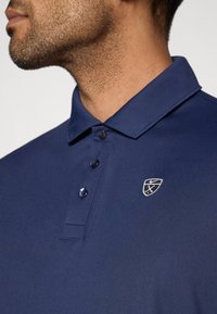 Πόλο μπλούζα σε ναυτικό μπλε χρώμα με κλασικό γιακά, σειρά με τρία κουμπιά και κεντημένο λογότυπο στο αριστερό μέρος. Ομαλό, διαπνέον ύφασμα.