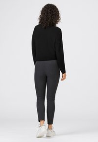 Svart stickad tröja i kombination med mörkgrå leggings, som visar en figurnära design. Vita sneakers fulländar outfitten. Texturen är synlig.