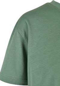 Gros plan d’un T-shirt vert en coton à manches courtes montrant la couture de l’épaule et une partie de la manche.
