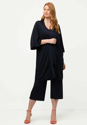 Námořnický kardigan ve stylu kimono z lehké látky s širokými rukávy, kombinovaný s námořnickými culottes a oranžovými sandály na podpatku. Hladká textura, volný střih.