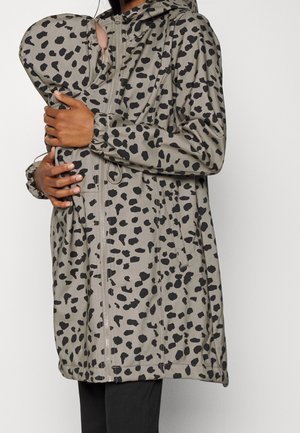 Persoon met een grijze jas met zwarte luipaardvlekken, die een baby vasthoudt die vastzit in een bijpassende draagjas met capuchon en rits.