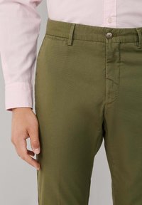 Pantalones de algodón verde oliva con frente plano, bolsillos planos y cierre de botón. Presentan un corte recto y textura suave.