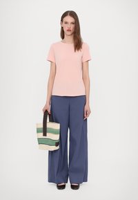 Lys rosa kortermet t-skjorte, kombinert med vide blå bukser. Modellen holder en stripete beige og grønn tote bag med mørk håndtak.
