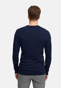 Granatowy sweter dzianinowy z wzorem w warkocze, okrągłym dekoltem oraz ściągaczami przy mankietach i dolnej krawędzi. Materiał wygląda na miękki z teksturowaną powierzchnią.