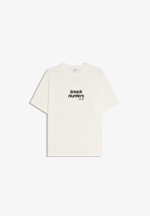 T-shirt bianca a maniche corte con testo nero "Snack Hunters est. '96" centrato sul davanti, sfondo semplice.