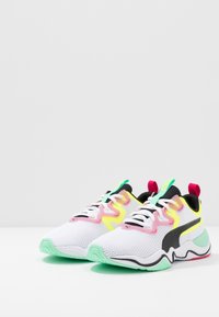 Weiße Laufschuhe mit Obermaterial aus Netzgewebe, schwarzen und pastellfarbenen Akzenten, grünen und rosafarbenen Details sowie einer strukturierten Sohle. Verfügt über ein auffälliges Schnürdesign.