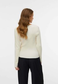 Maglione a coste crema con maniche lunghe e scollatura rotonda, abbinato a pantaloni neri a gamba larga. Tessuto liscio e design aderente.