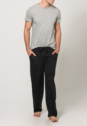 Graues T-Shirt mit kurzen Ärmeln, kombiniert mit schwarzen Jogginghosen mit Kordelzug, die eine lockere Passform und glatte Textur aufweisen, barfuß auf einem hellen Hintergrund stehend.