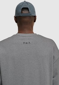 Grijze sweatshirt met ronde hals, voorzien van een gedrukt "F.U.T."-logo op de achterkant. De stof heeft een gladde textuur en een casual pasvorm.