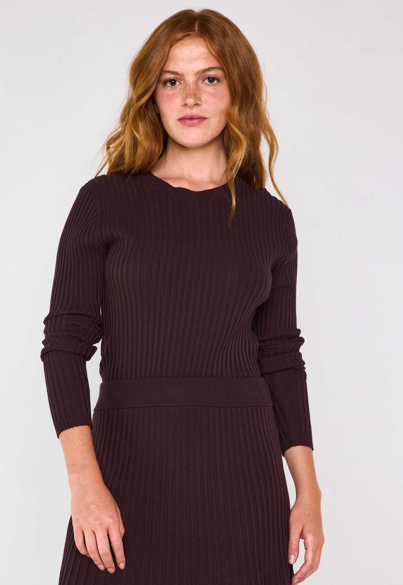 Vestito a maglia a coste di colore viola scuro, con scollatura rotonda e maniche lunghe. Il tessuto presenta un aspetto testurizzato ed una silhouette aderente.