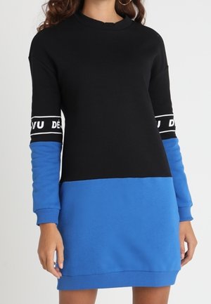 Robe sweat noire et bleue avec des manches longues, un col rond, des lettres noires en gras sur les poignets et un design en blocs de couleurs.