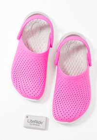 Sabots perforés roses avec une forme arrondie et une semelle blanche. Présente une sangle au talon réglable et une semelle intérieure texturée. Comprend une étiquette avec un logo.