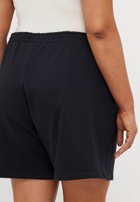 Juodi medvilniniai šortai su elastinga juosmeniu. Audinys yra lygus ir šiek tiek tamprus, su šoninėmis siūlėmis ir laisvu siluetu.