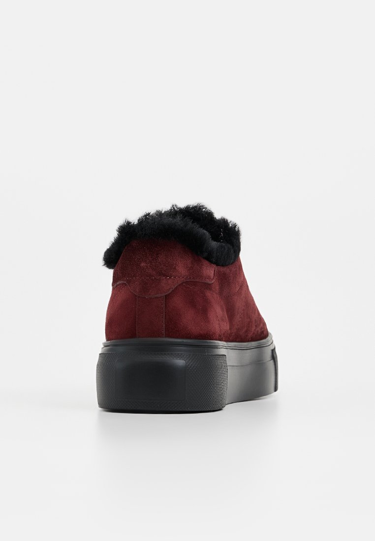 Burgundowe zamszowe sneakersy z czarnym kołnierzem z sztucznego futra, grubą czarną gumową podeszwą i gładką fakturą, prezentujące elegancki, zaokrąglony kształt.