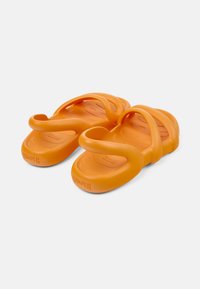Oranssi kumisaappaat, joissa on muotoiltu muotoilu, kaksi paksua, kiertävää rihmaa ja teksturoitu pohja mukavuutta varten.