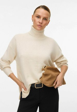 Pull en col roulé beige en maille douce, avec des épaules tombantes, associé à un sacoche en daim marron et une ceinture noire avec une boucle dorée.