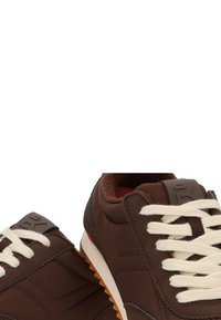 Zapatos deportivos marrones hechos de material sintético, con cordones blancos, lados texturizados y suela de goma con un acento marrón.