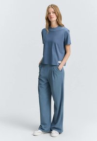 Modrý top s krátkými rukávy z bavlněné směsi s volnějším střihem, doplněný o odpovídající široké kalhoty s jemnými záhyby a designem délky ke kotníkům.