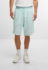 Lyseblå teksturerede shorts med elastisk talje og snor-detalje. Har et geometrisk mønster på stoffet. Stylet med hvide sneakers.