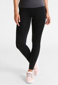 Zwarte sportlegging met textuur en een diamantpatroon op de bovenbenen, met een aansluitend ontwerp. Gecombineerd met lichtroze hardloopschoenen.