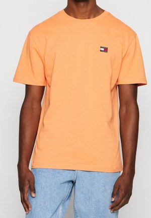 Kortärmad orange bomulls-T-shirt med rund hals, med en liten Tommy Jeans-logopatch på vänster bröst. Slät textur.