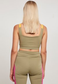 Olivengrønn crop top med gule stropper, kombinert med matchende leggings med rosa sidestykker; glatt, elastisk stoff, tettsittende design.