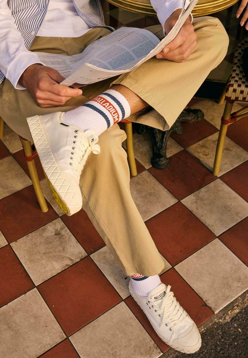 Valkoiset kangastennarit teksturoiduilla kumipohjilla, yhdistettyinä valkoisiin urheilusukkiin, joissa on siniset ja oranssit raidat, käytetty beigenväristen chinojen kanssa.